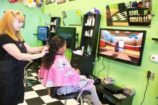 Hair stylist Cassie Briggs performs a cut and style while her client plays on a Playstation 3 at Sharkey's Cuts for Kids, a Henderson based hair salon for childen, Monday July 15, 2013.
